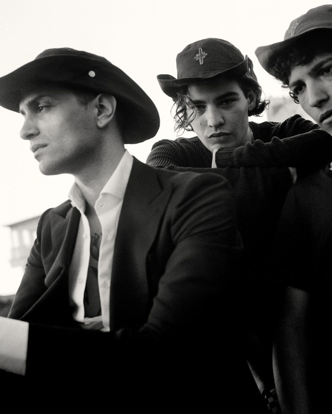 Three young men in vintage hats and clothing pose in an undated black and white photograph with a bright, out of focus background.