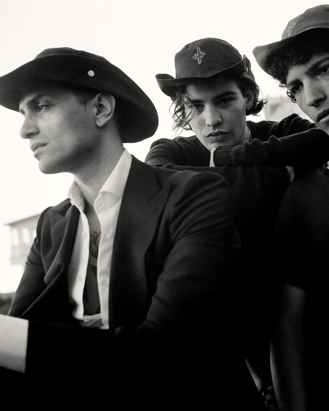 Three young men in hats and dark attire photographed in a black and white portrait by Brett Lloyd.