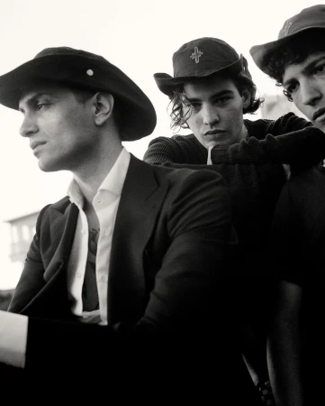 Three young men in hats and dark attire photographed in a black and white portrait by Brett Lloyd.