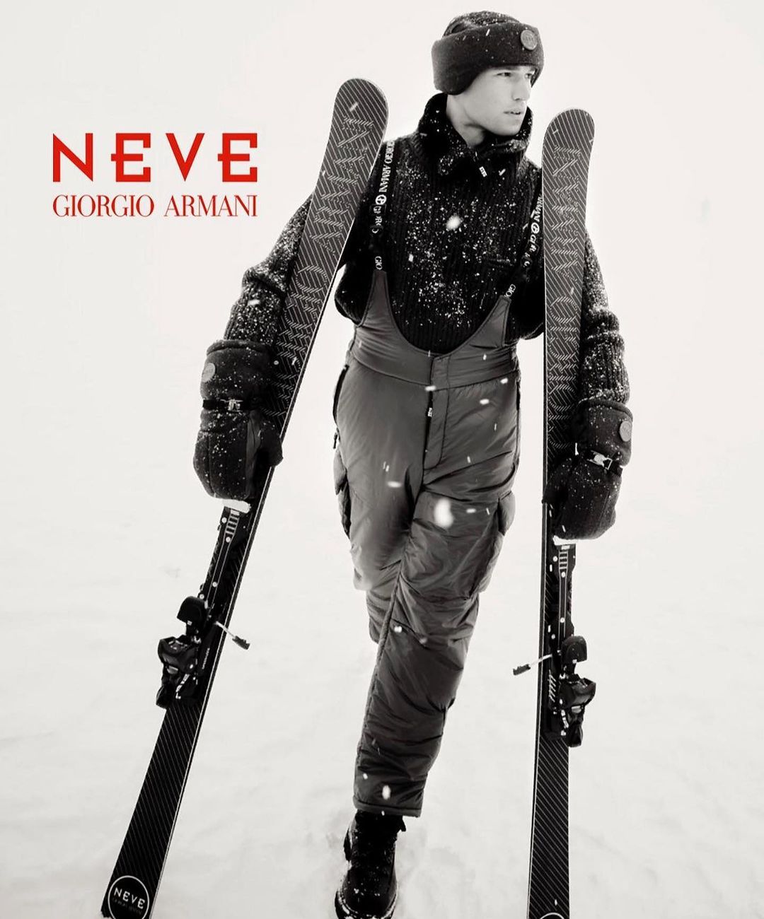 Fashion advertisement for Giorgio Armani Neve featuring a man in snow apparel holding skis in a snowy environment, showcasing winter fashion.