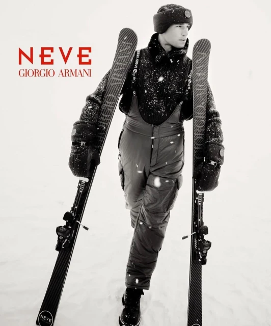 Fashion advertisement for Giorgio Armani Neve featuring a man in snow apparel holding skis in a snowy environment, showcasing winter fashion.