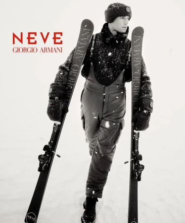 Fashion advertisement for Giorgio Armani Neve featuring a man in snow apparel holding skis in a snowy environment, showcasing winter fashion.