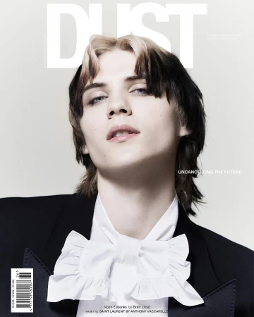 Magazine cover featuring a young adult with light skin, styled black and blonde hair, wearing a black blazer and white ruffled shirt.