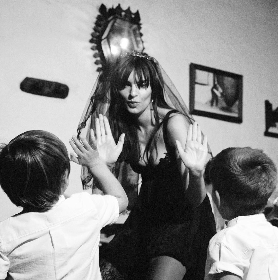 Black and white portrait of a woman in a veil interacting with two children indoors, creating a captivating visual narrative.