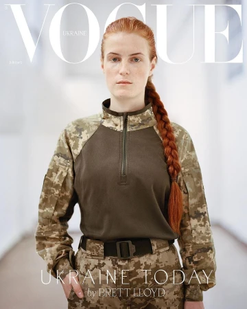 Vogue Ukraine cover featuring a red-haired woman in military uniform with a braid, standing indoors against a blurred hallway background.