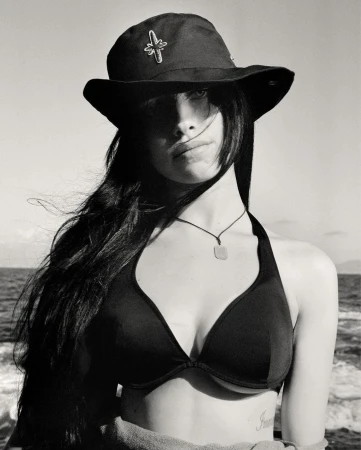 Black and white portrait of a young woman wearing a hat and bikini top on a boat, with the ocean and sky in the background.