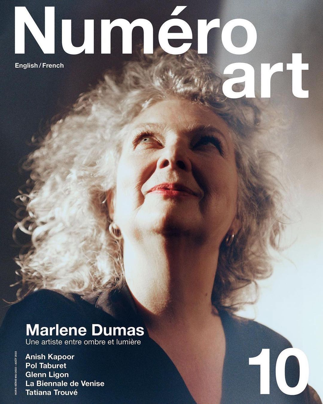 Magazine cover featuring an up-angle portrait of a smiling woman with voluminous gray hair, against a dark backdrop with diffused light.
