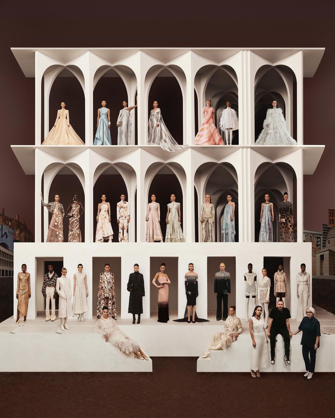 Fashion show featuring diverse models wearing a variety of elegant gowns and dresses, staged on a tiered white platform with arches.