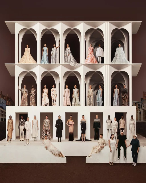 Fashion show featuring diverse models wearing a variety of elegant gowns and dresses, staged on a tiered white platform with arches.