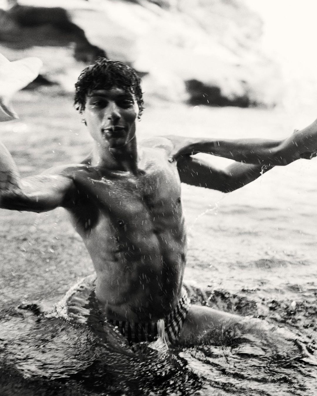 Black and white portrait of a shirtless young man wading in water with splashing droplets captured by Brett Lloyd.