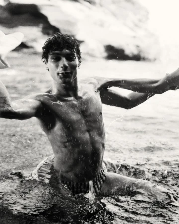 Black and white portrait of a shirtless young man wading in water with splashing droplets captured by Brett Lloyd.
