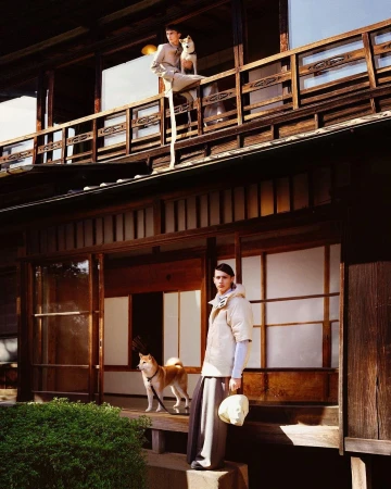 Two Shiba Inu dogs with a male fashion model wearing modern clothing on a traditional Japanese building's balcony and porch.