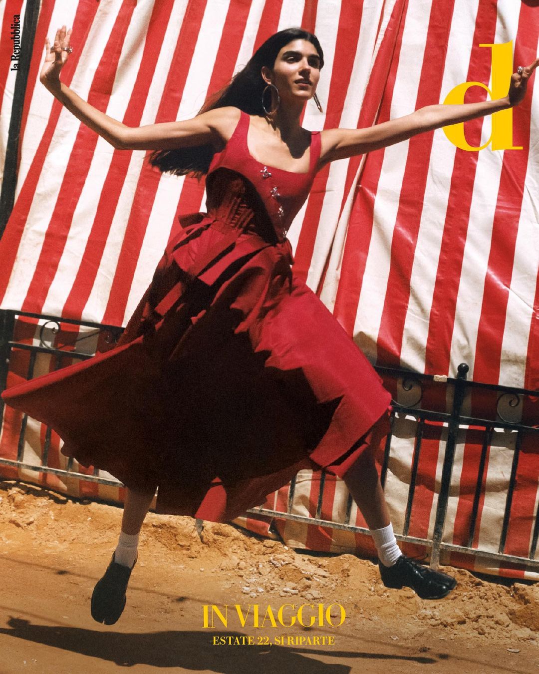 A woman in a red dress is joyfully leaping in the air, arms outstretched, with a red and white striped awning in the background.
