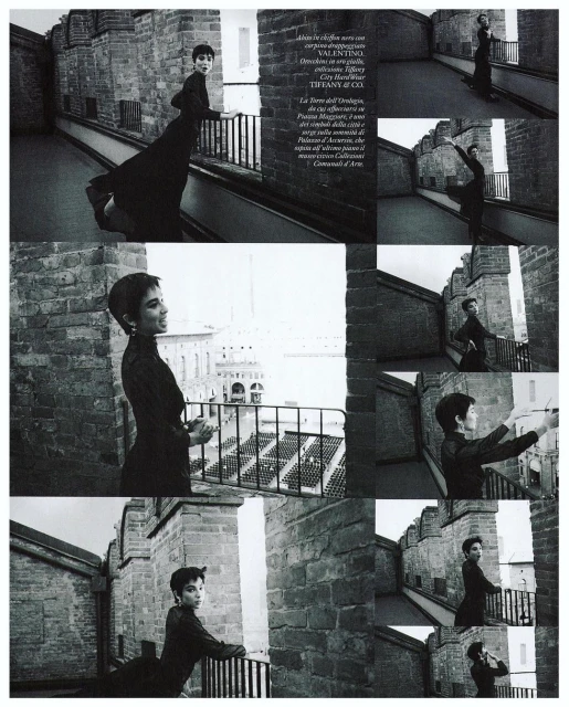 Woman in elegant dress poses on castle turret overlooking city. Editorial fashion shot with historical architecture and monochromatic color.