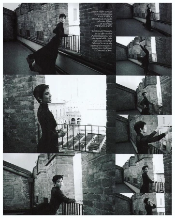 Woman in elegant dress poses on castle turret overlooking city. Editorial fashion shot with historical architecture and monochromatic color.