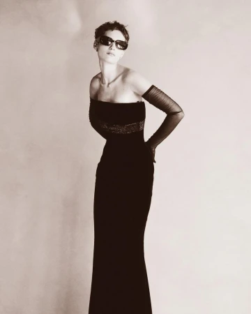 Model with short hair wearing sunglasses and a black strapless evening gown with sheer opera gloves