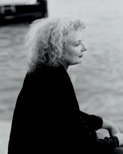 Monochrome portrait of a mature adult female with curly hair in profile, gazing at the water and natural light in an outdoor setting.
