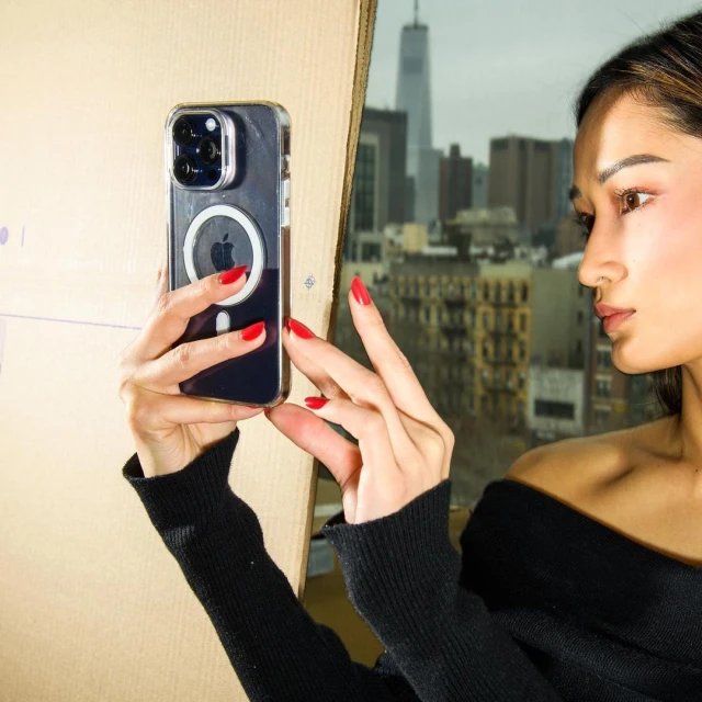 Woman takes a photo of a city view with an iPhone. The woman is wearing a black sweater and red nail polish.