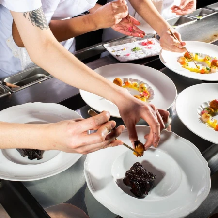 Chefs plating gourmet dishes with artistic food arrangement in a professional kitchen setting, using tweezers and fine dining techniques.