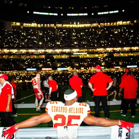 Football player in uniform stands in stadium with a cheering crowd and bright lights during an evening football game.