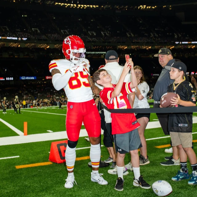 American football player poses for a photo with a boy on the football field. Sports fan holds a football in the stadium.