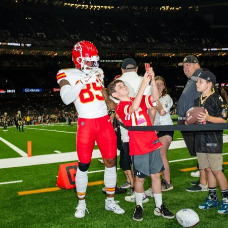 American football player poses for a photo with a boy on the football field. Sports fan holds a football in the stadium.