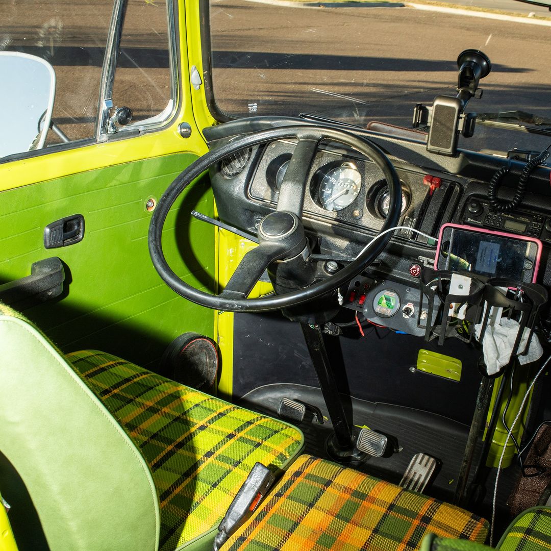 Interior of a vintage yellow van featuring a black steering wheel, green and yellow plaid seats, dashboard instruments, and a retro design.