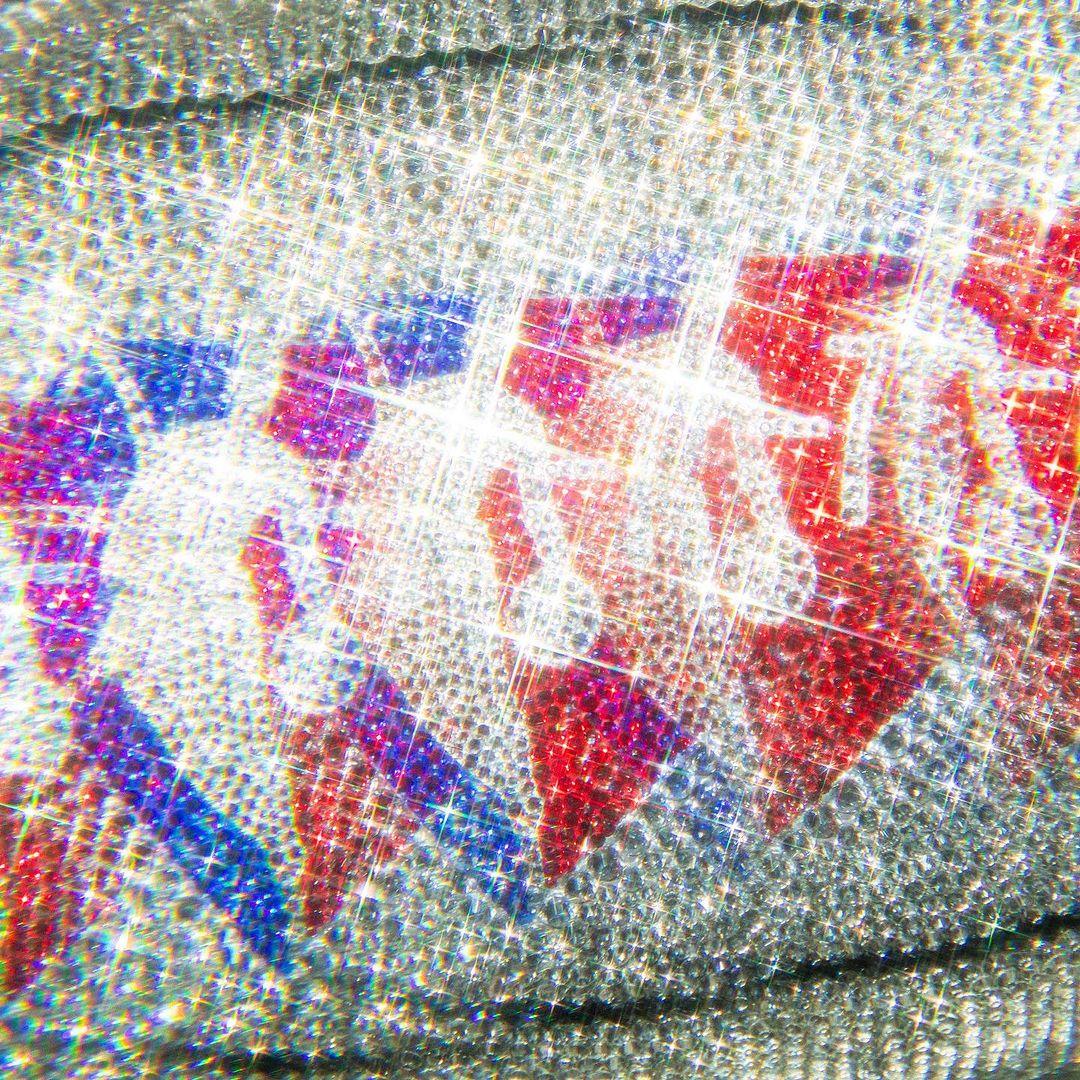 Close-up of a shimmering fabric with repeating red, white, and blue triangle shapes, creating a sparkling, textured, and vibrant visual.