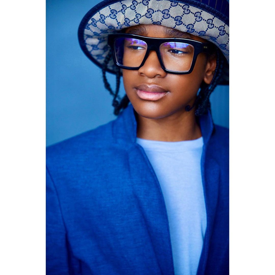Stylish portrait of an African-American child wearing a designer bucket hat and black glasses, looking off to the side.