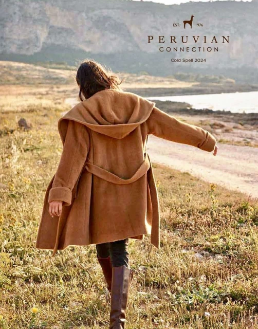 Woman in a hooded tan coat walks through a grassy field on a sunny day. Advertisement for Peruvian Connection's Cold Spell 2024 collection.