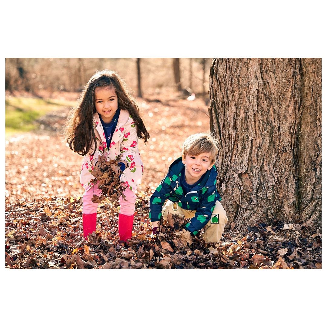 A girl and a boy are playing in a forest with dry leaves in autumn. The children are smiling. They are holding the dry leaves.