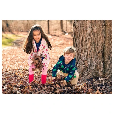 A girl and a boy are playing in a forest with dry leaves in autumn. The children are smiling. They are holding the dry leaves.
