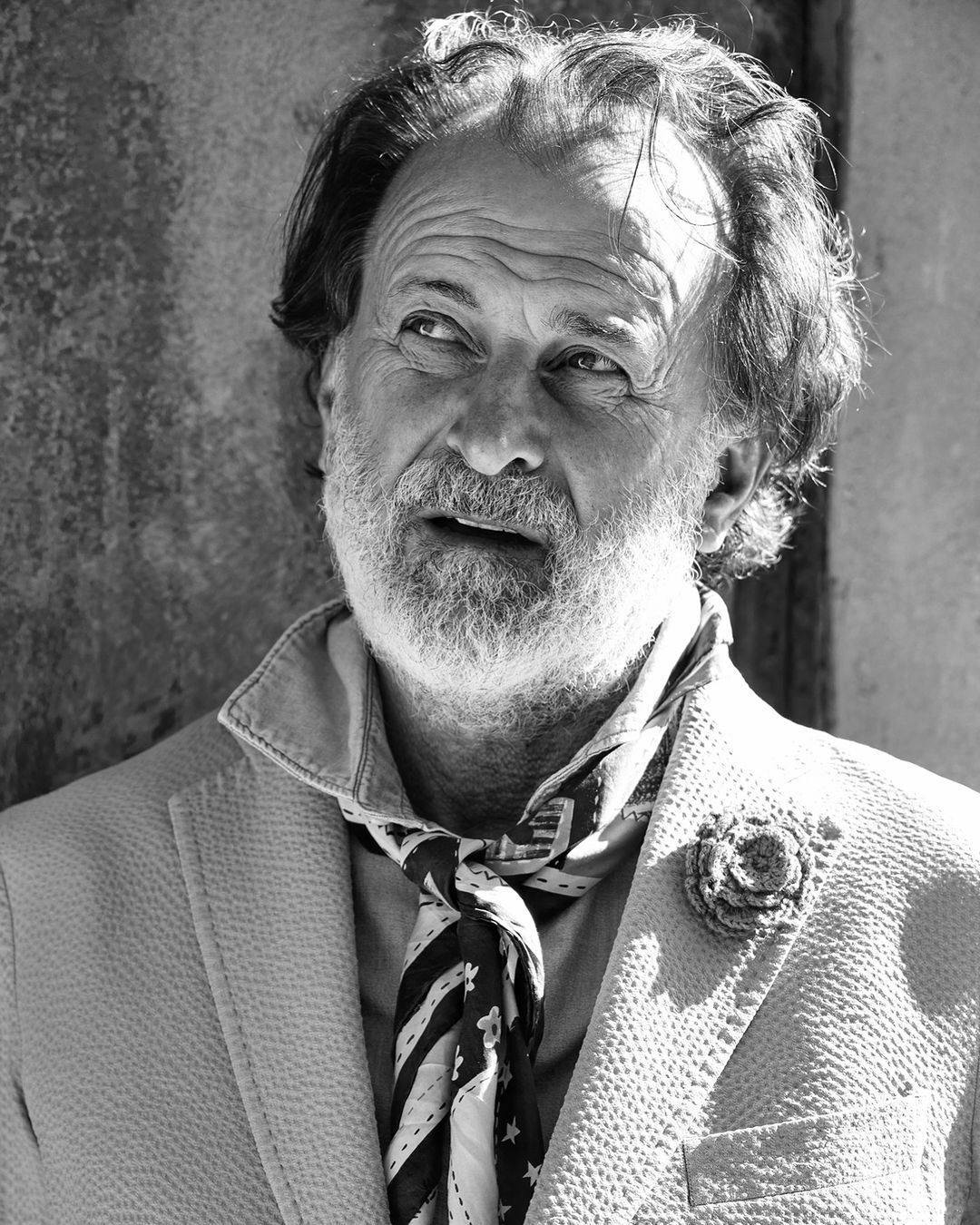 Black and white portrait of an older man with a beard wearing a patterned neck scarf and textured blazer.