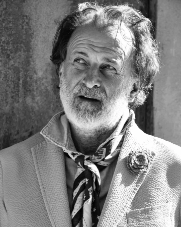 Black and white portrait of an older man with a beard wearing a patterned neck scarf and textured blazer.
