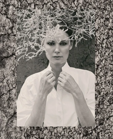 Monochrome portrait of an adult female in a button-down shirt with frosty branches overhead, set against a textured, cracked backdrop.