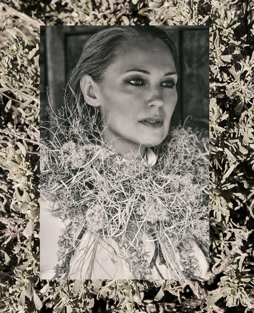 Monochrome portrait of an adult female surrounded by dried foliage against a neutral background, creating a natural, textured aesthetic.