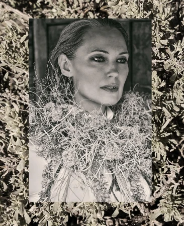Monochrome portrait of an adult female surrounded by dried foliage against a neutral background, creating a natural, textured aesthetic.