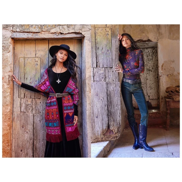 Two women posing in front of rustic wooden doors, one in a colorful shawl and the other in jeans and boots in soft, diffused light.
