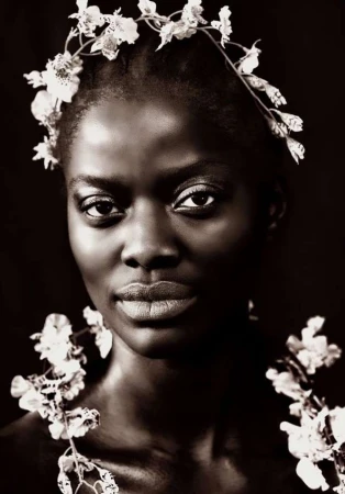 Portrait of a black woman wearing a floral headband and flower garlands against a dark background, photographed by Brian Sassmann.