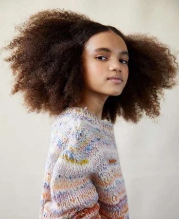 Portrait of a young African American girl with natural afro hair wearing a multicolored knit sweater against a neutral background.