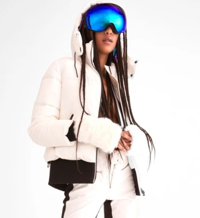 Model wearing a white puffer jacket and iridescent blue ski goggles against a seamless white background.