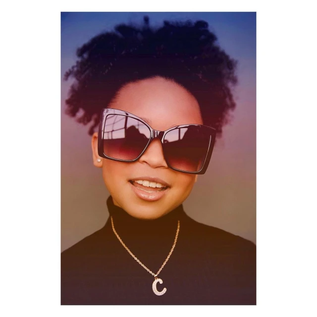 Portrait of a young African-American woman wearing a black turtleneck and oversized sunglasses, with a gold initial pendant necklace.