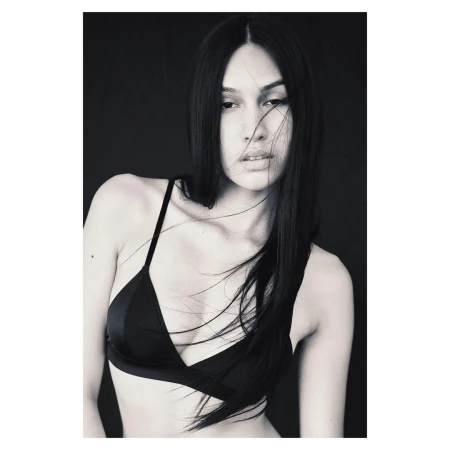 Black and white portrait of a woman with long dark hair wearing a dark bra top against a dark background