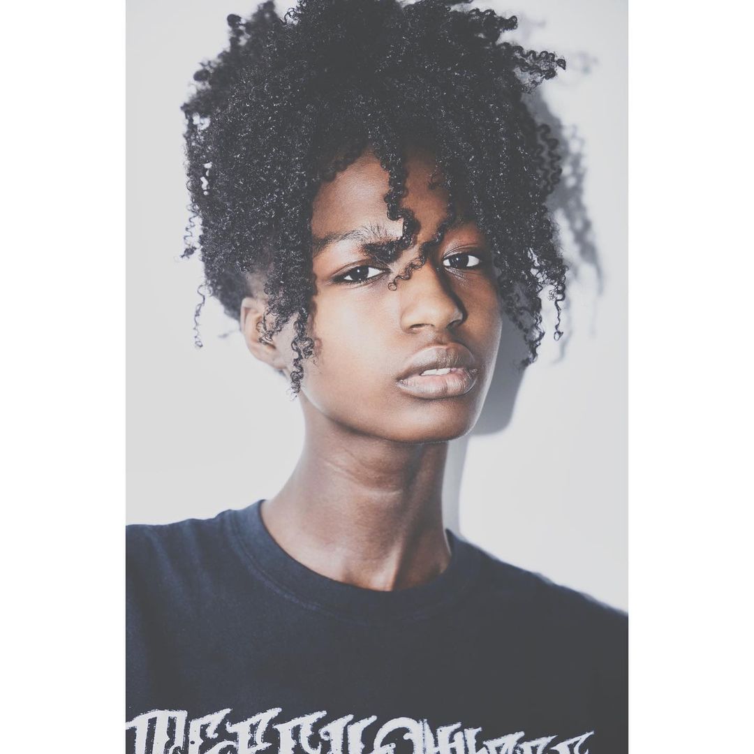Portrait of a young black woman with curly hair wearing a dark t-shirt against a plain white background by Brian Sassmann