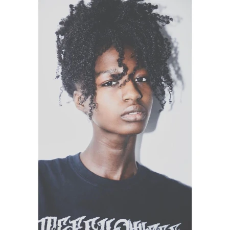 Portrait of a young black woman with curly hair wearing a dark t-shirt against a plain white background by Brian Sassmann