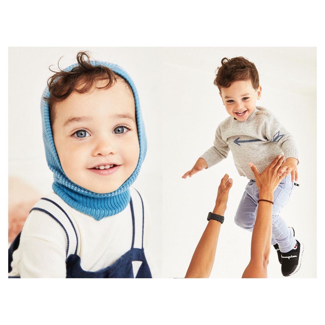 Two young children smile cheerfully. One wears a blue balaclava, and the other is thrown into the air by adult hands.