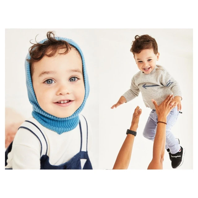 Two young children smile cheerfully. One wears a blue balaclava, and the other is thrown into the air by adult hands.