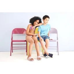 Boy and girl sitting on colourful folding chairs against a pale neutral background in studio portrait by Brian Sassmann