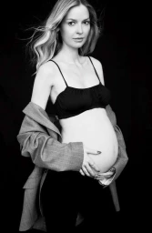 Pregnant woman wearing a black bralette and draped grey blazer against a dark background in New York.