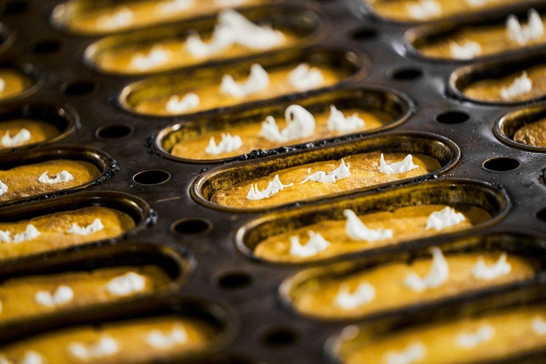 Close-up of a baking tray filled with rows of golden brown sponge cakes, each topped with a dollop of white cream frosting.